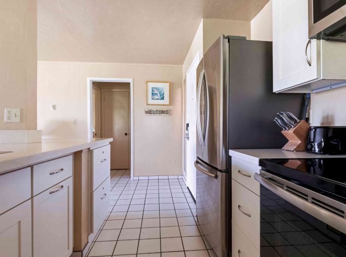 A modern kitchen featuring white cabinets, stainless steel refrigerator, black stove, microwave, countertop with knife block, and tiled floor.