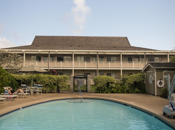 A large outdoor pool with clear water is in front of a multi-story building that has a A-frame roof and balconies.