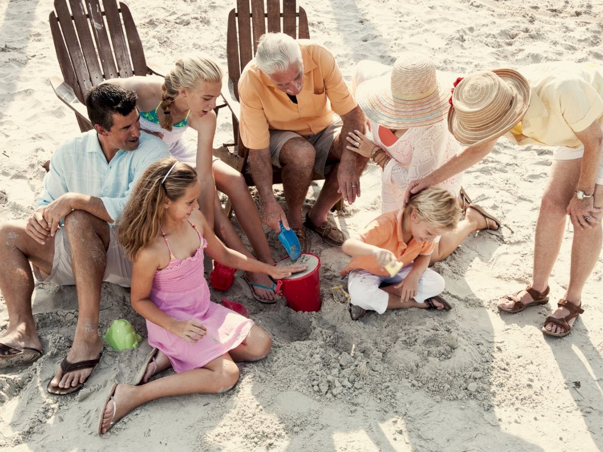 A group of people enjoying time together on a sandy beach, with some building sandcastles and others watching or sitting on chairs.