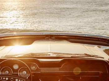 A convertible car parked near the coastline, overlooking an ocean view at sunrise or sunset, with its top down and a scenic horizon.