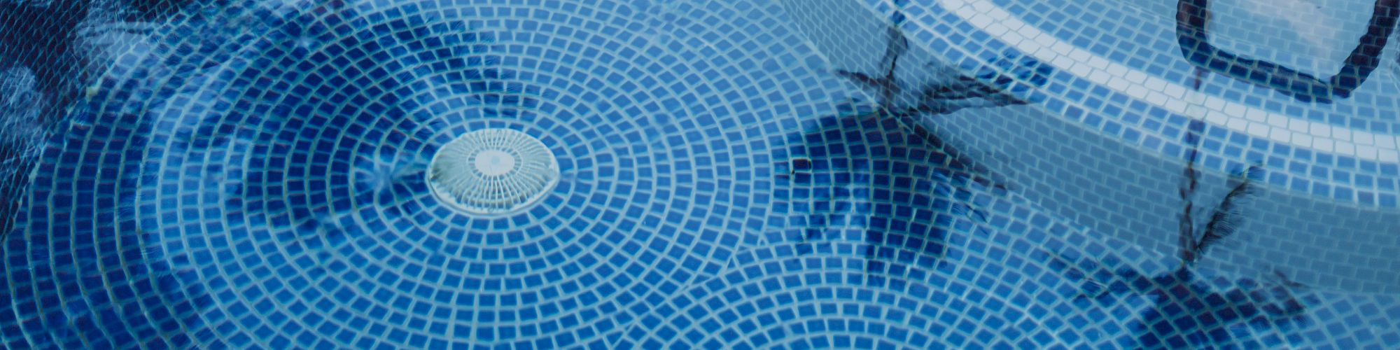 The image shows the clear water of a circular swimming pool with blue mosaic tiles, reflecting palm trees and the sky above, creating a serene scene.